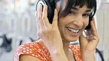 A woman an orange flower dress smiling about what she is hearing via her headphones