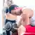 Mulher com barriga musculosa observa homem sentado exercitando o bíceps com halteres